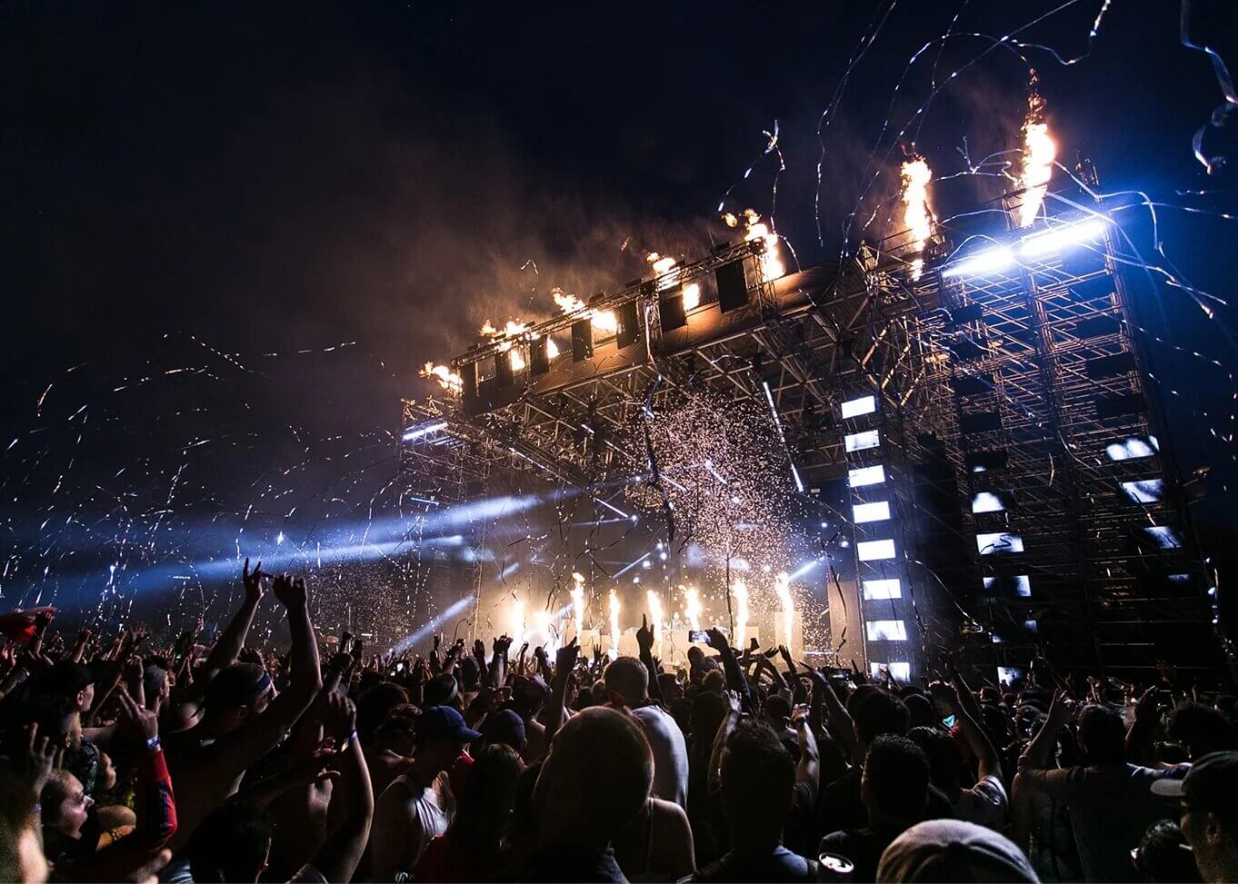A large stage with lights and pyrotechnics in front of a huge crowd