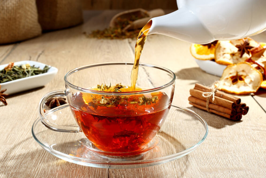 Tea is poured from a teapot into a clear teacup.