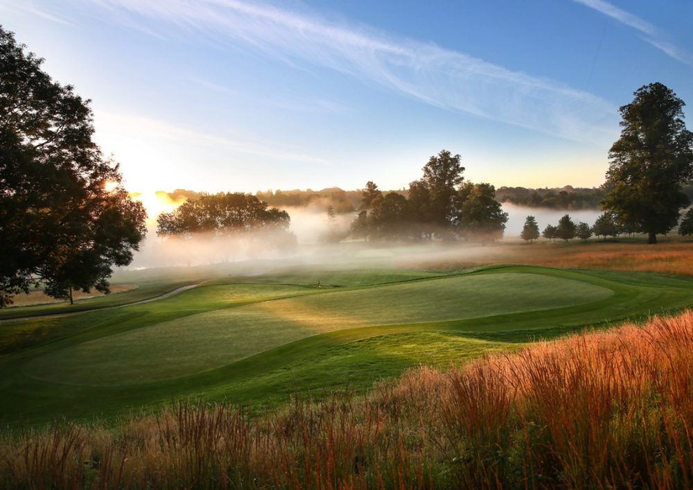 Image of a golf course with blue skies and mist.