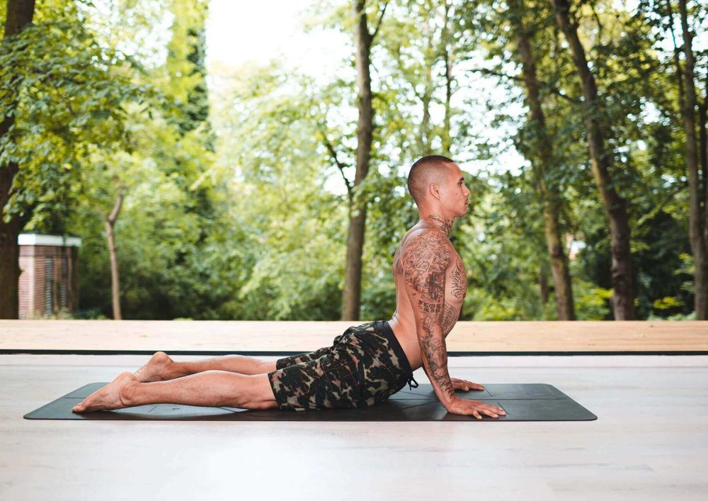 A man doing yoga on a mat with trees in the background.