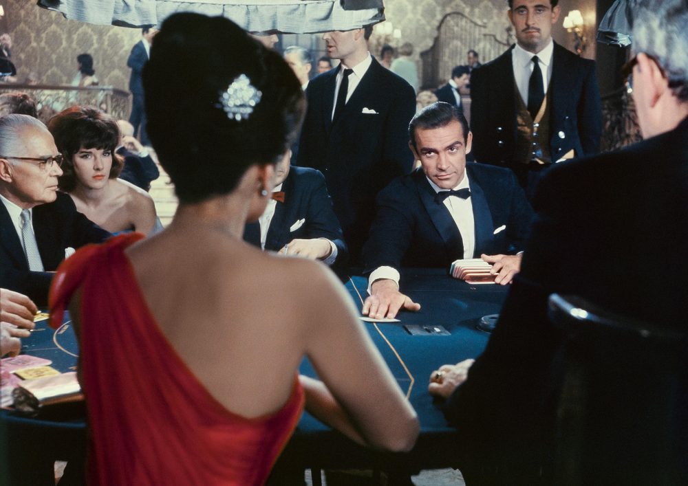 James Bond in Mayfair Casino placing a card down and looking at a woman.