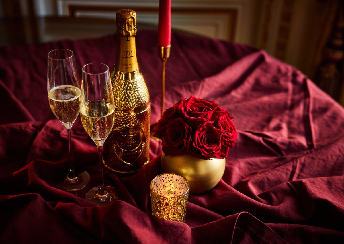 2 glasses of champagne, 1 bottle, roses, and a candle on a red table cloth.