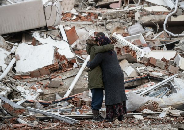 Grieving women hugging next to a collapsed building in Syria.