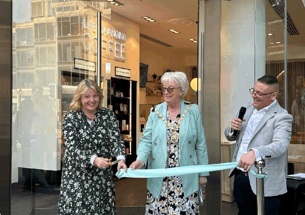 Three people standing outside of Change Please Coffee, holding a ribbon